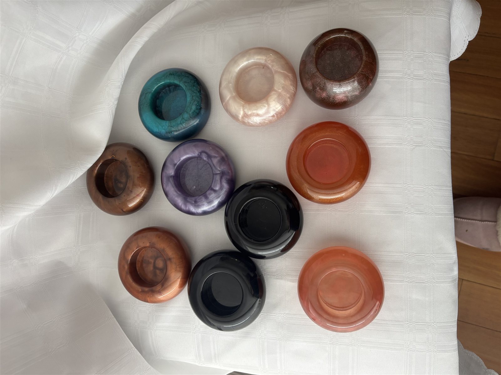Ten small round resin ring dishes in a range of colours, laid out on white linen