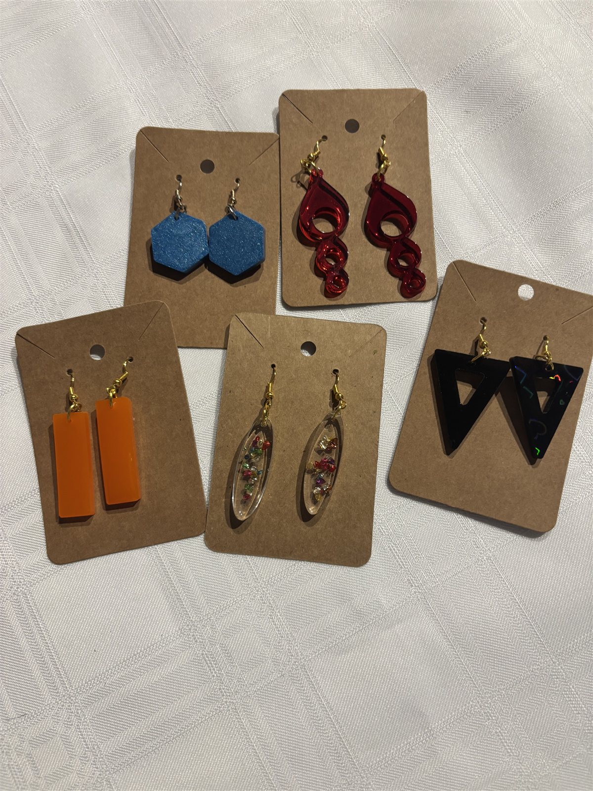 Five pairs of resin drop earrings on cards, hexagon, spiral, rectangle, oval and triangle shapes