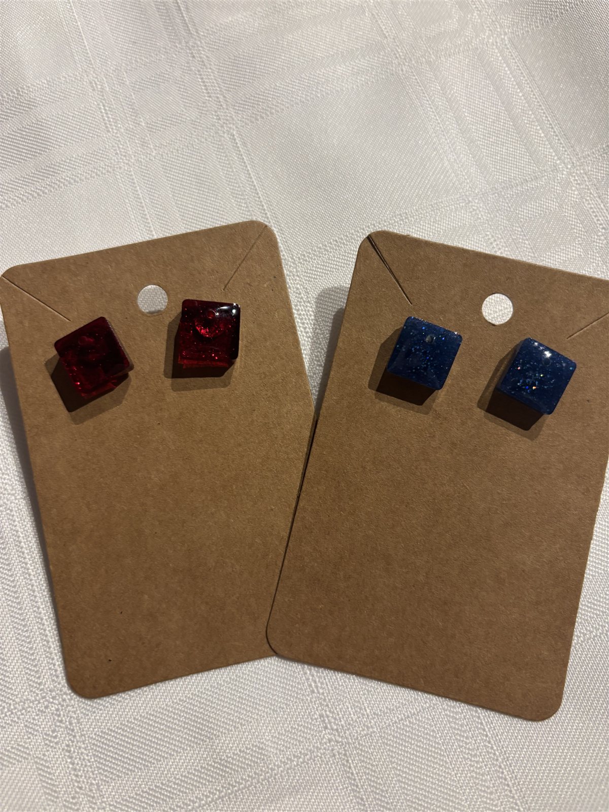 Two pairs of small square resin stud earrings on cards, red and blue glitter