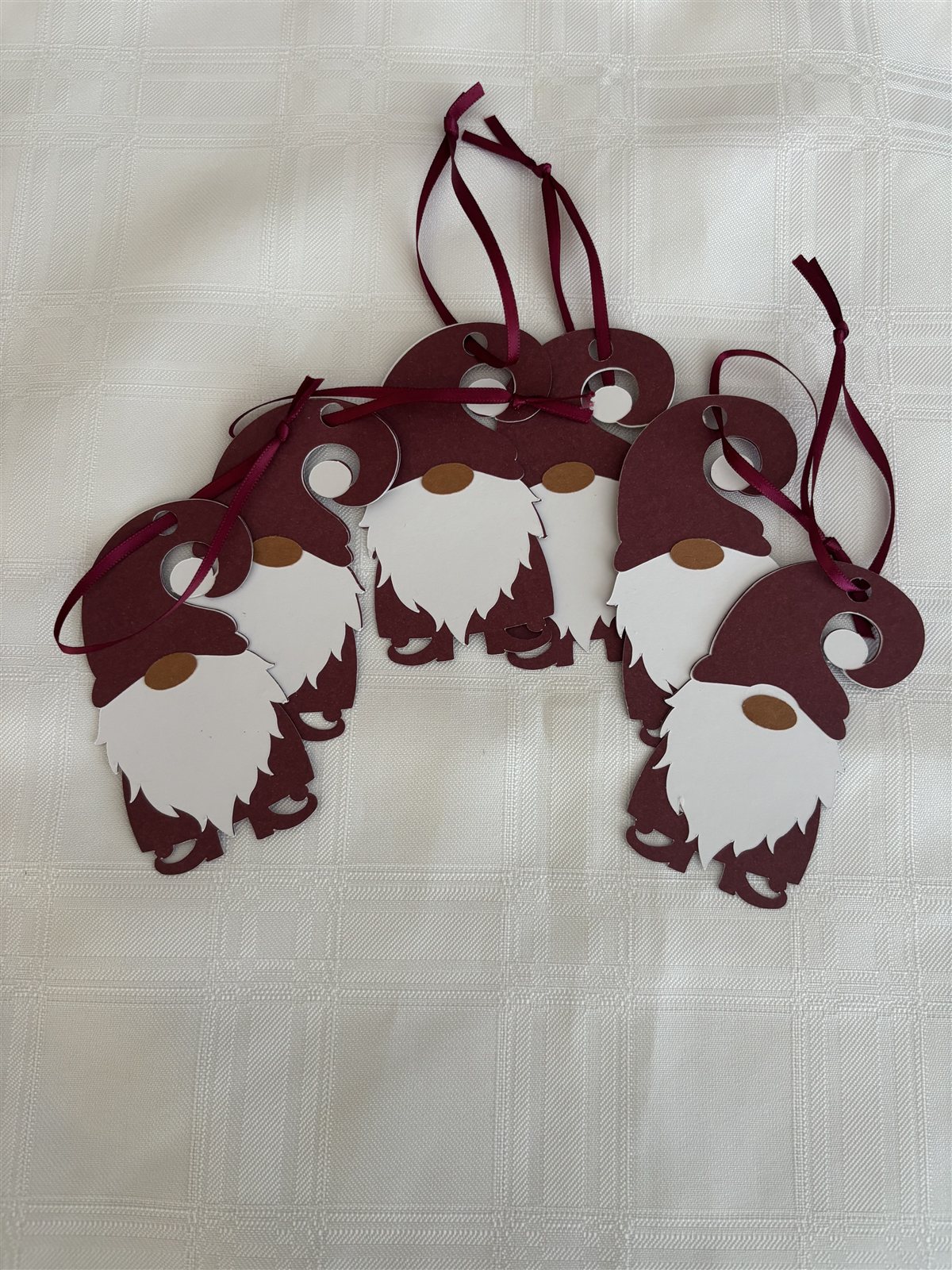Six burgundy gnome-shaped gift tags with white beards and burgundy ribbon