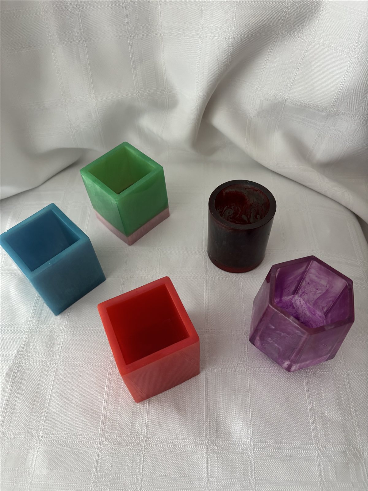 Five small geometric resin candle holders, cubes, a hexagon and a round shape, in purple, red, green, blue and dark red