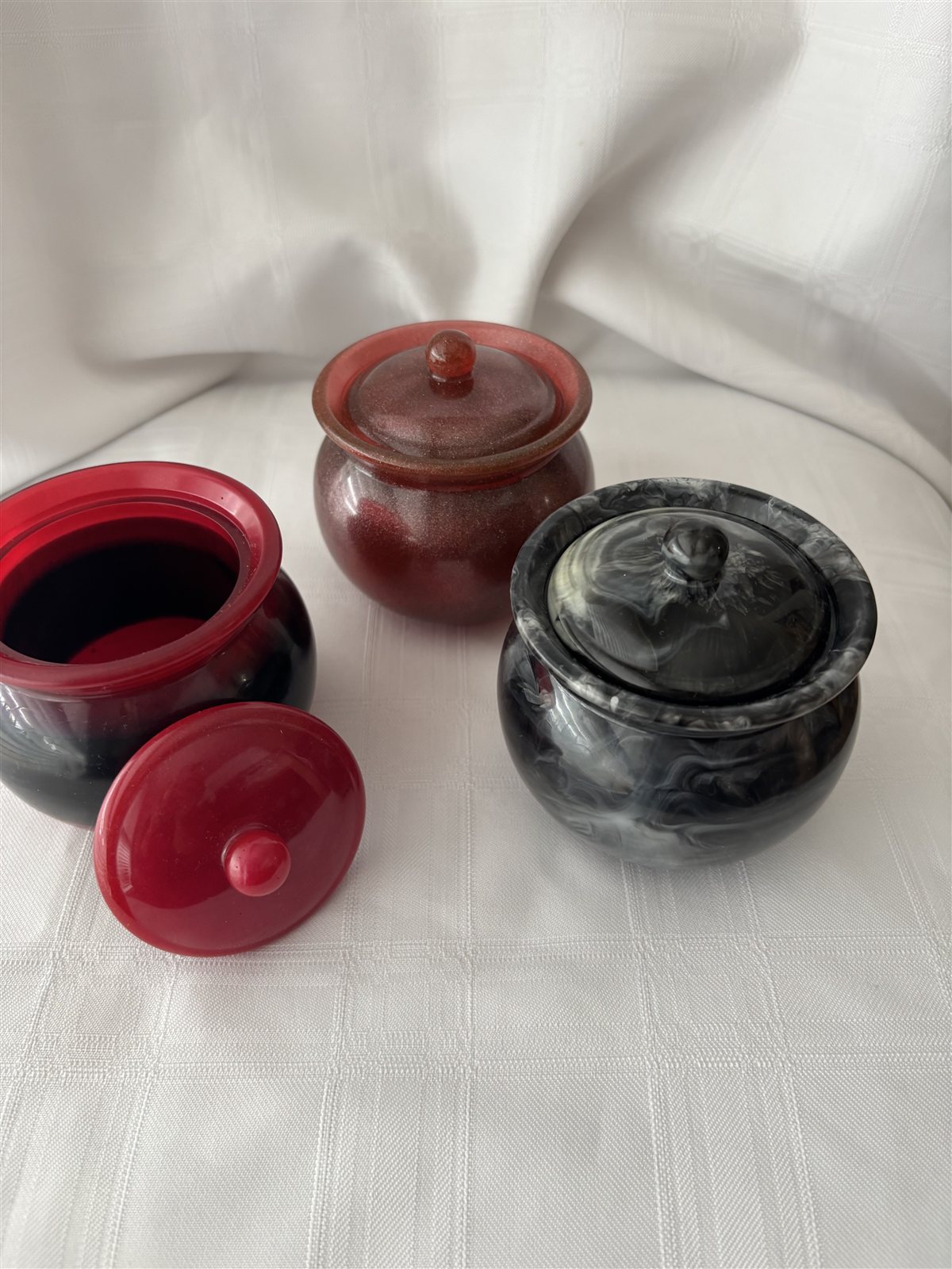 Three round lidded resin jars with knob handles, in black marble, red and deep red