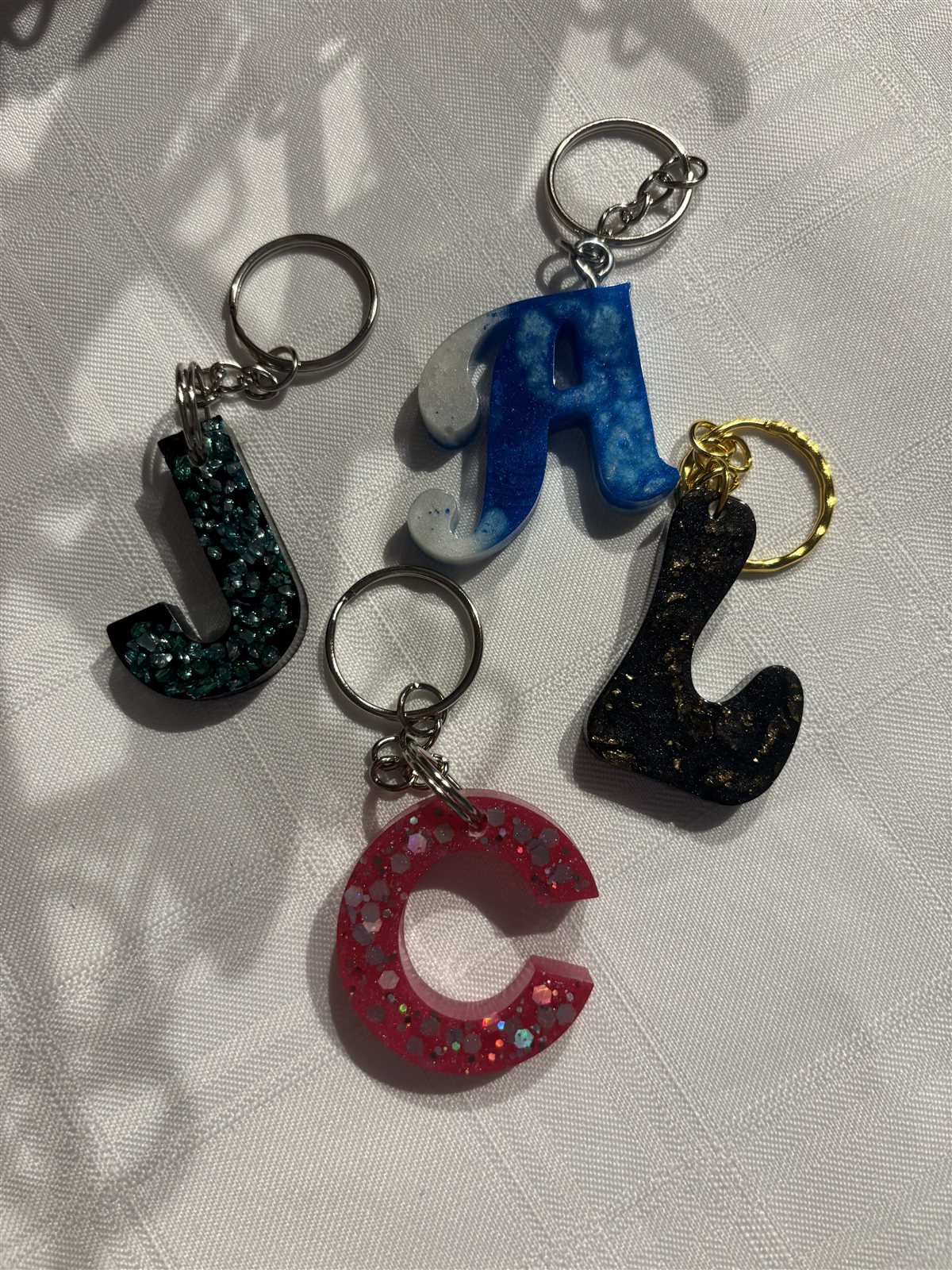 Four resin letter keychains, J, A, L and C, in different colours and finishes
