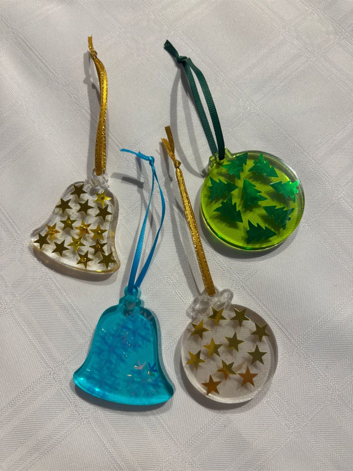 Four resin Christmas ornaments on ribbon, a gold star bell, a blue snowflake bell, a green tree bauble and a gold star bauble