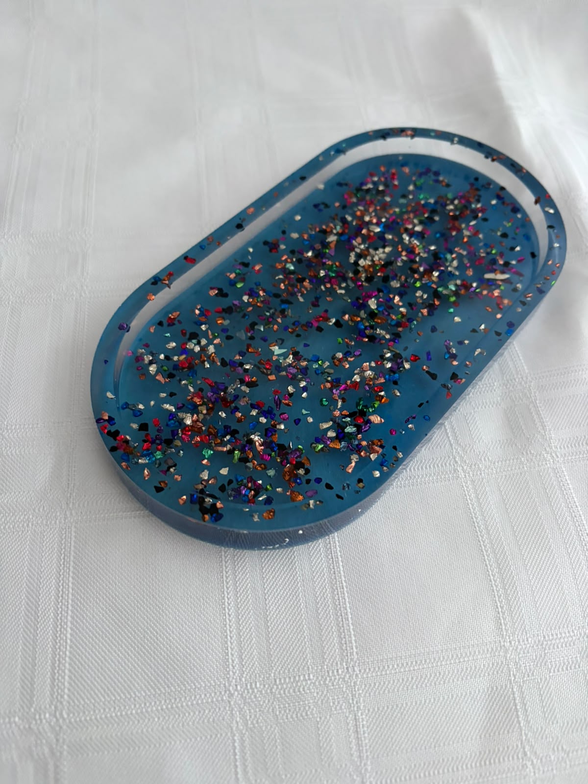 Oval blue resin tray filled with multicoloured metallic flake